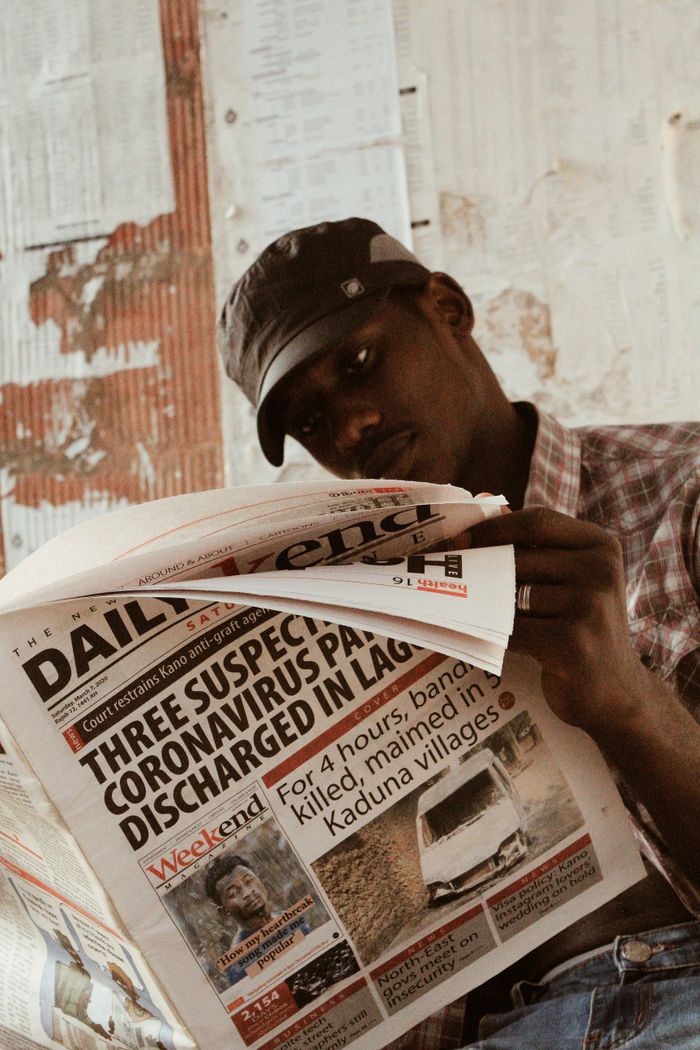 Casually dressed man reading a newspaper indoors, focusing on headlines.